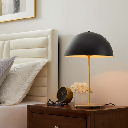 Black dome bedside lamp with brass stem on dark wood nightstand, beside a clock, glasses and white flowers.