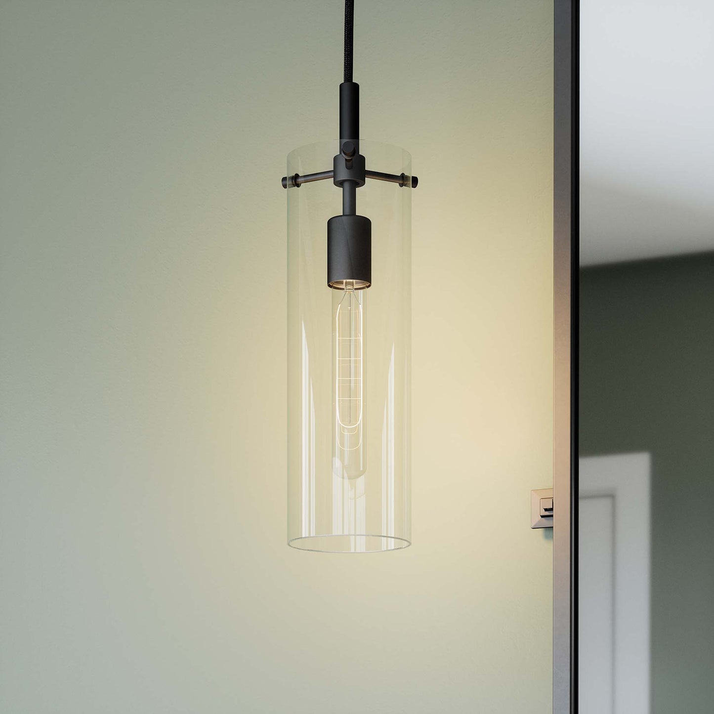 Clear glass cylindrical pendant light with black metal hardware and Edison filament bulb.