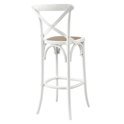 White metal bar stool with X-back, woven natural rattan seat, curved legs and footrest; industrial farmhouse style.