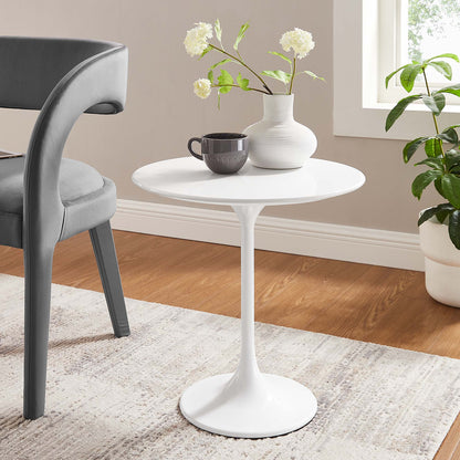 White round pedestal table with a tulip-style base, in a cozy room with a vase of flowers and a mug.