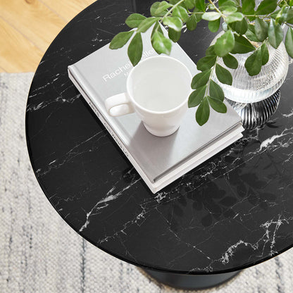 Round faux marble side table with a white mug, a gray book, and a glass vase of green leaves.