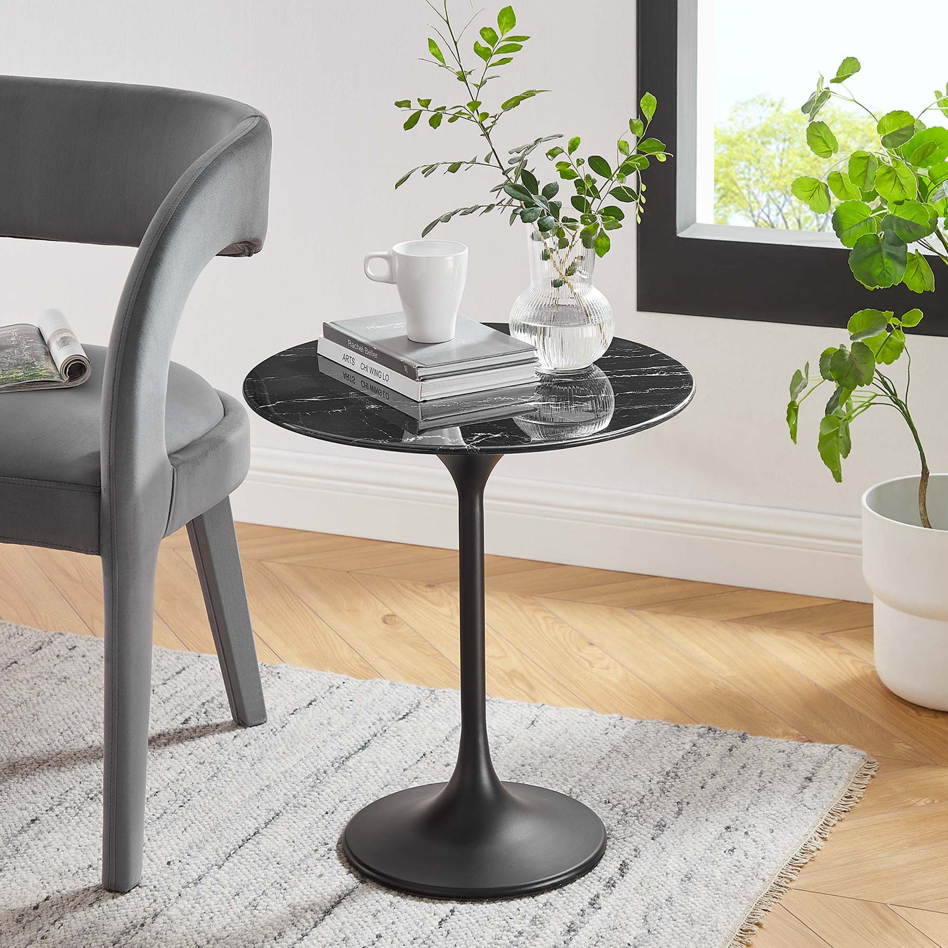 Round black marble-top pedestal side table with slim stem and circular base, paired with gray chair and plants.