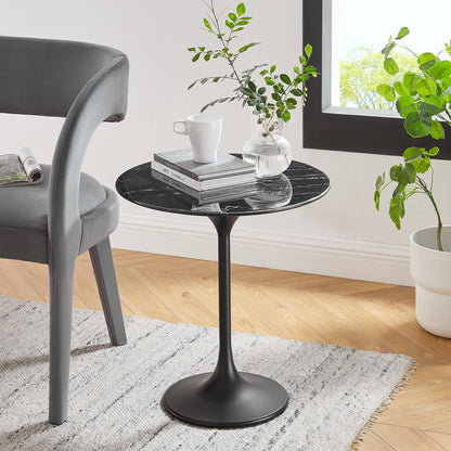 Round black marble-top pedestal side table with slim stem and circular base, paired with gray chair and plants.