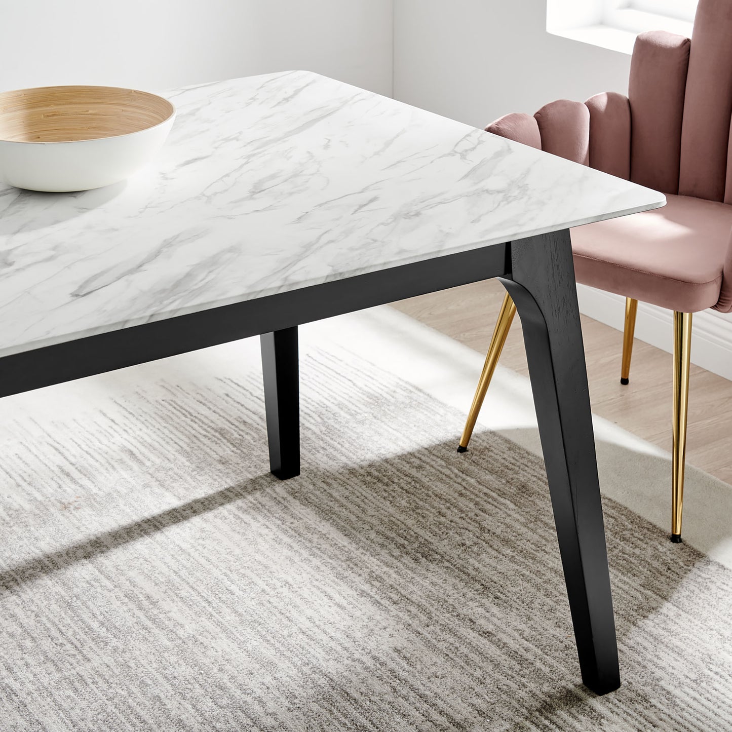 Modern rectangular dining table with white artificial marble top & black angled legs; pink velvet chair with gold legs.