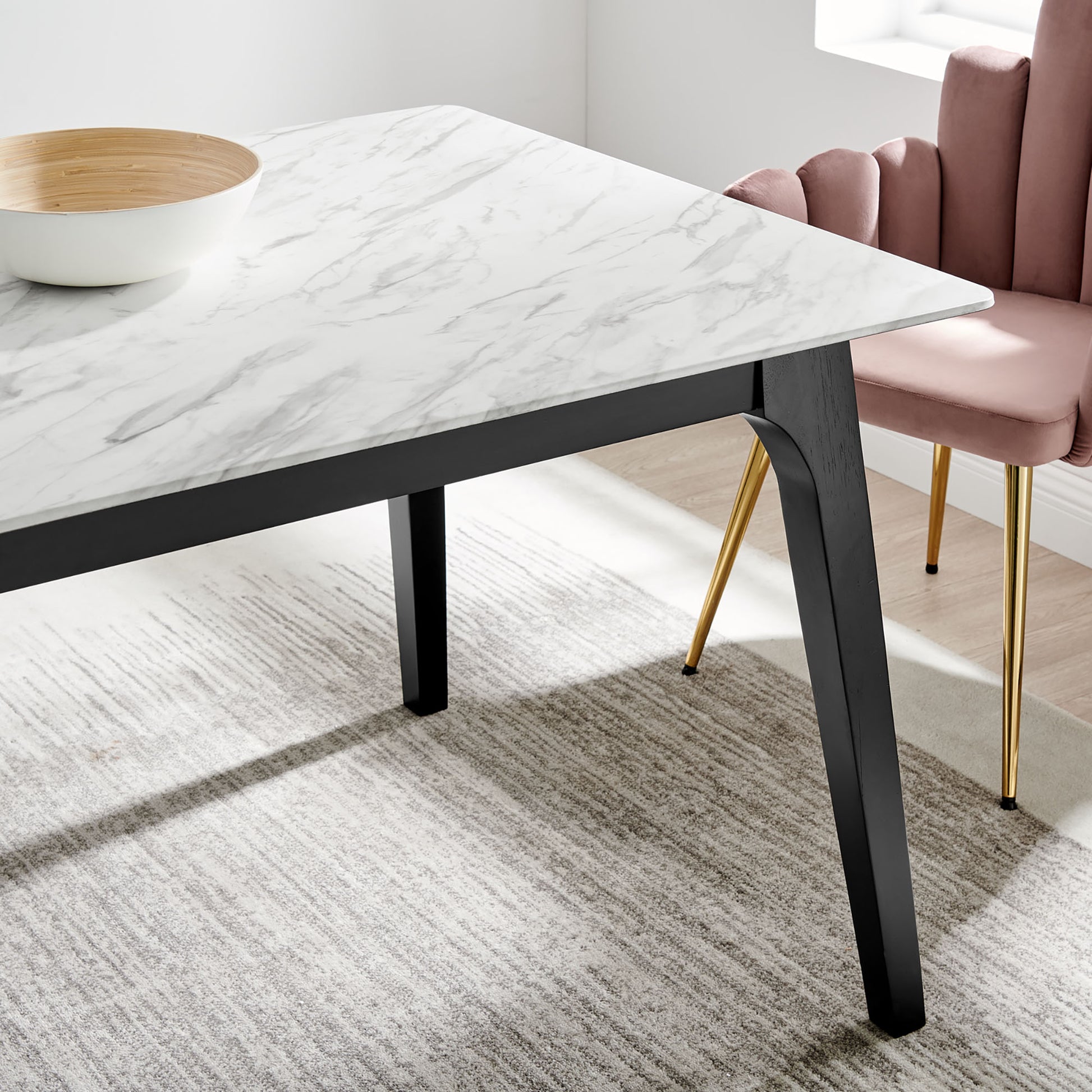 Modern rectangular dining table with white artificial marble top & black angled legs; pink velvet chair with gold legs.