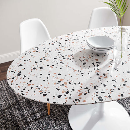 Oval terrazzo-white dining table with multicolor speckles, white chairs, plates and glass vase with plant.