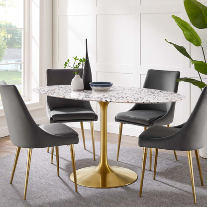 Oval terrazzo dining table with a white speckled top on a gold pedestal base, surrounded by gray upholstered chairs in a bright dining room.