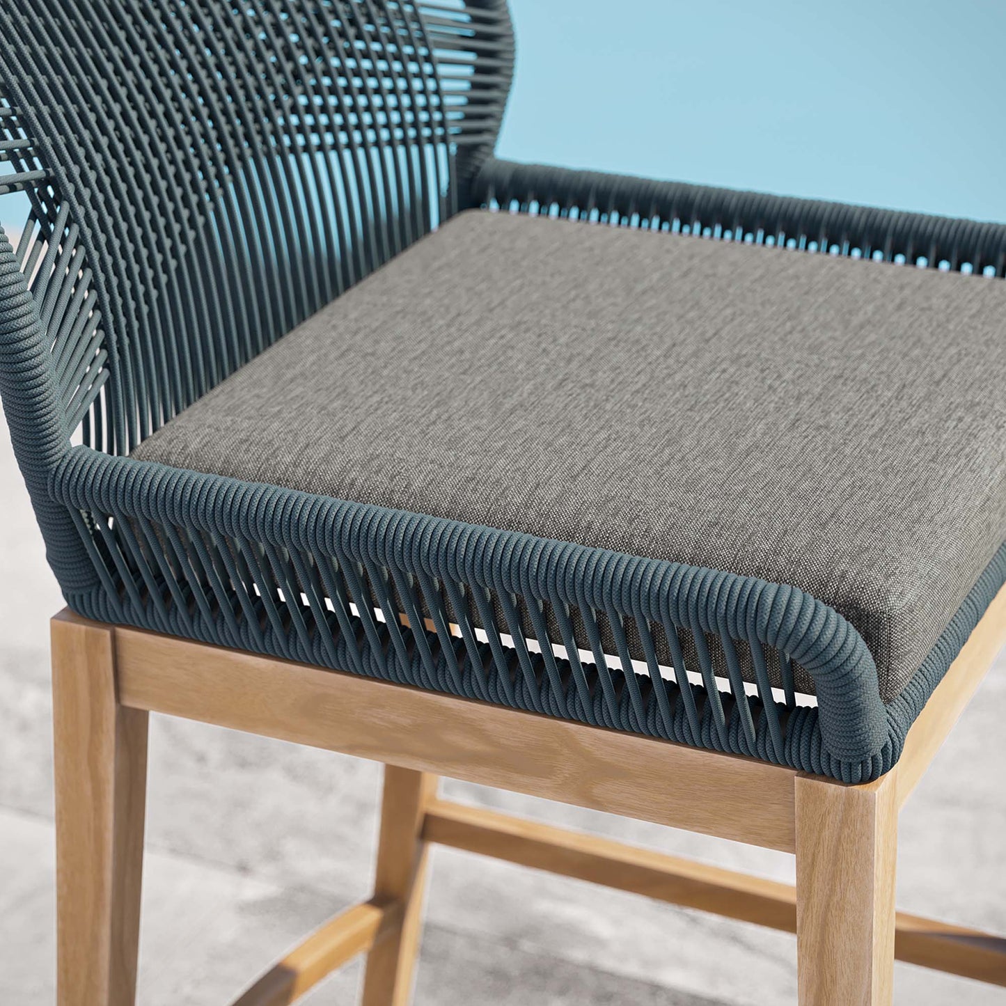 Blue woven rope outdoor teak wood bar stool with grey cushion.