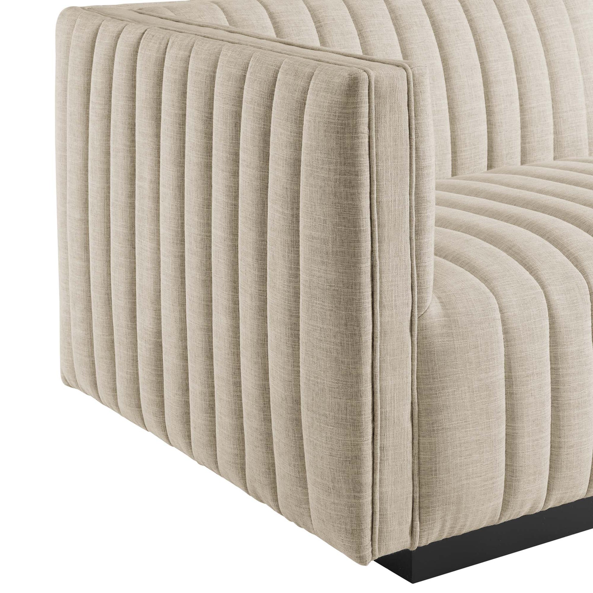 Beige fabric sofa with vertical channel tufting, square arms, and a low black rectangular base.