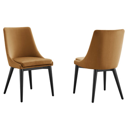Two caramel-brown velvet upholstered dining chairs with curved backs and black tapered legs, mid-century style.