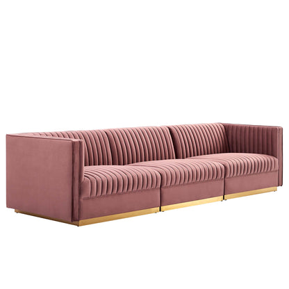 Red velvet sofa with vertical channel tufting, modular three-seat layout, low square arms and gold metal legs.