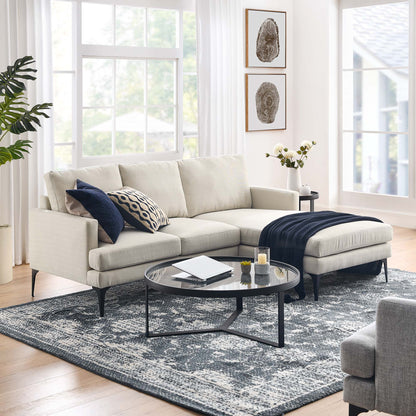 Beige sectional with chaise, navy throw, round glass coffee table; blue-gray patterned rug in a bright living room.