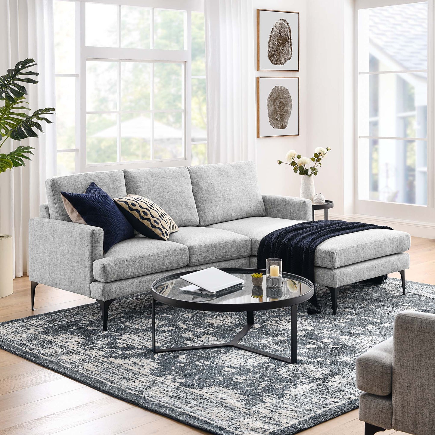 Light gray fabric sectional with chaise, navy throw, and patterned cushions; round glass coffee table on a blue-gray rug.