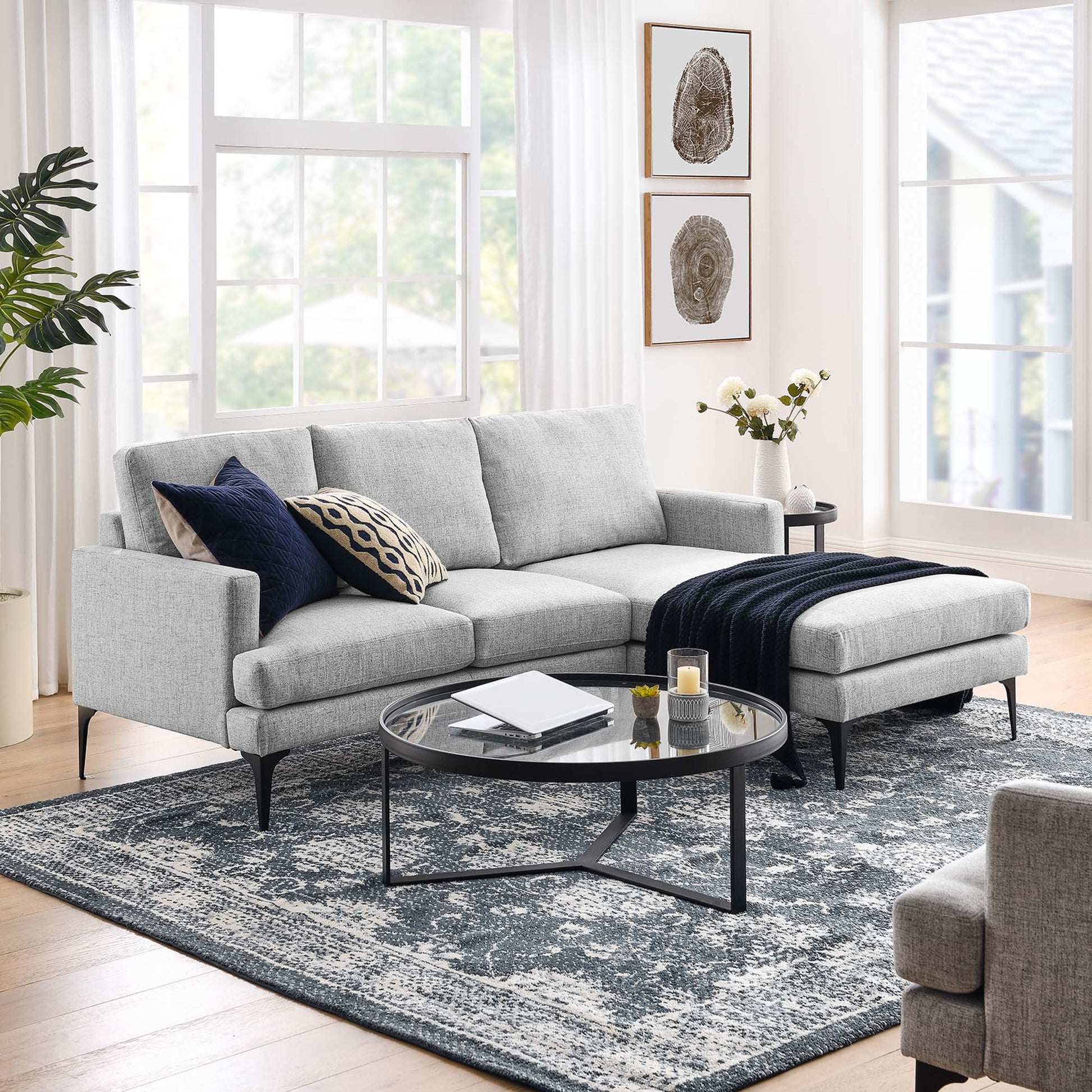 Light gray fabric sectional with chaise, navy throw, and patterned cushions; round glass coffee table on a blue-gray rug.