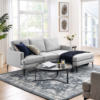 Light gray fabric sectional with chaise, navy throw, and patterned cushions; round glass coffee table on a blue-gray rug.