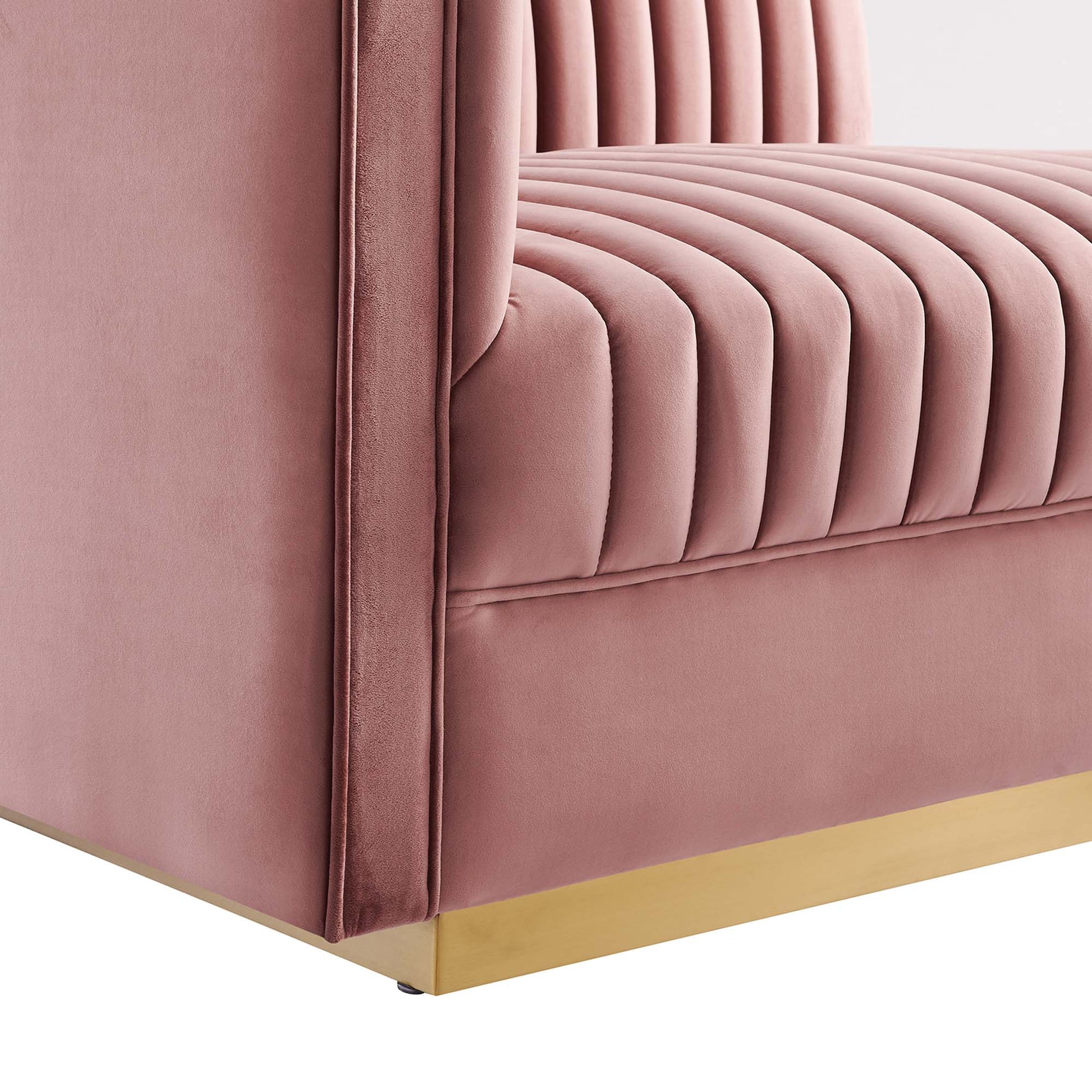 Rose-pink velvet sofa with vertical channel tufting and a gold metal base.