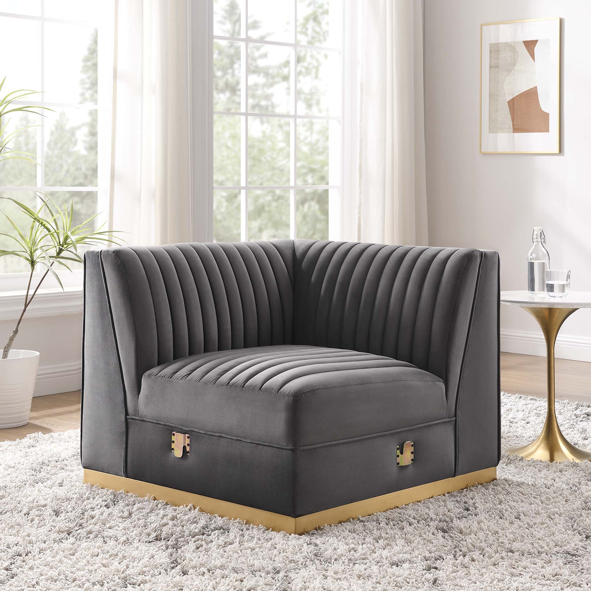 Gray velvet modular sectional sofa left corner chair with vertical channel tufting and gold-tone base trim in a bright living room.