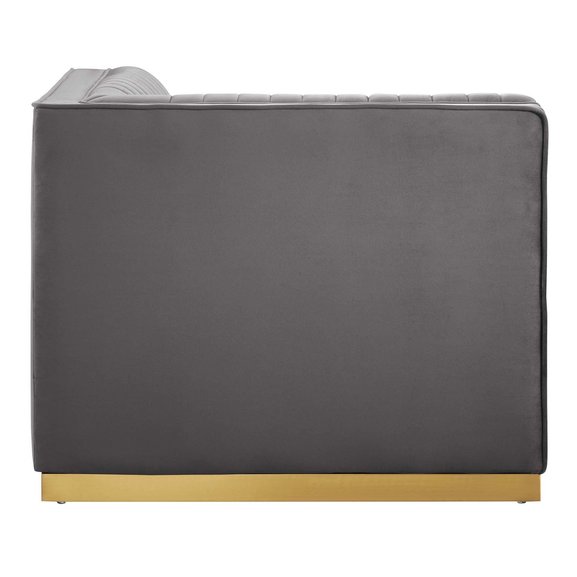 Grey velvet sofa with curved, ribbed headrest and gold-plated plinth base; modern, low-profile lounge style.