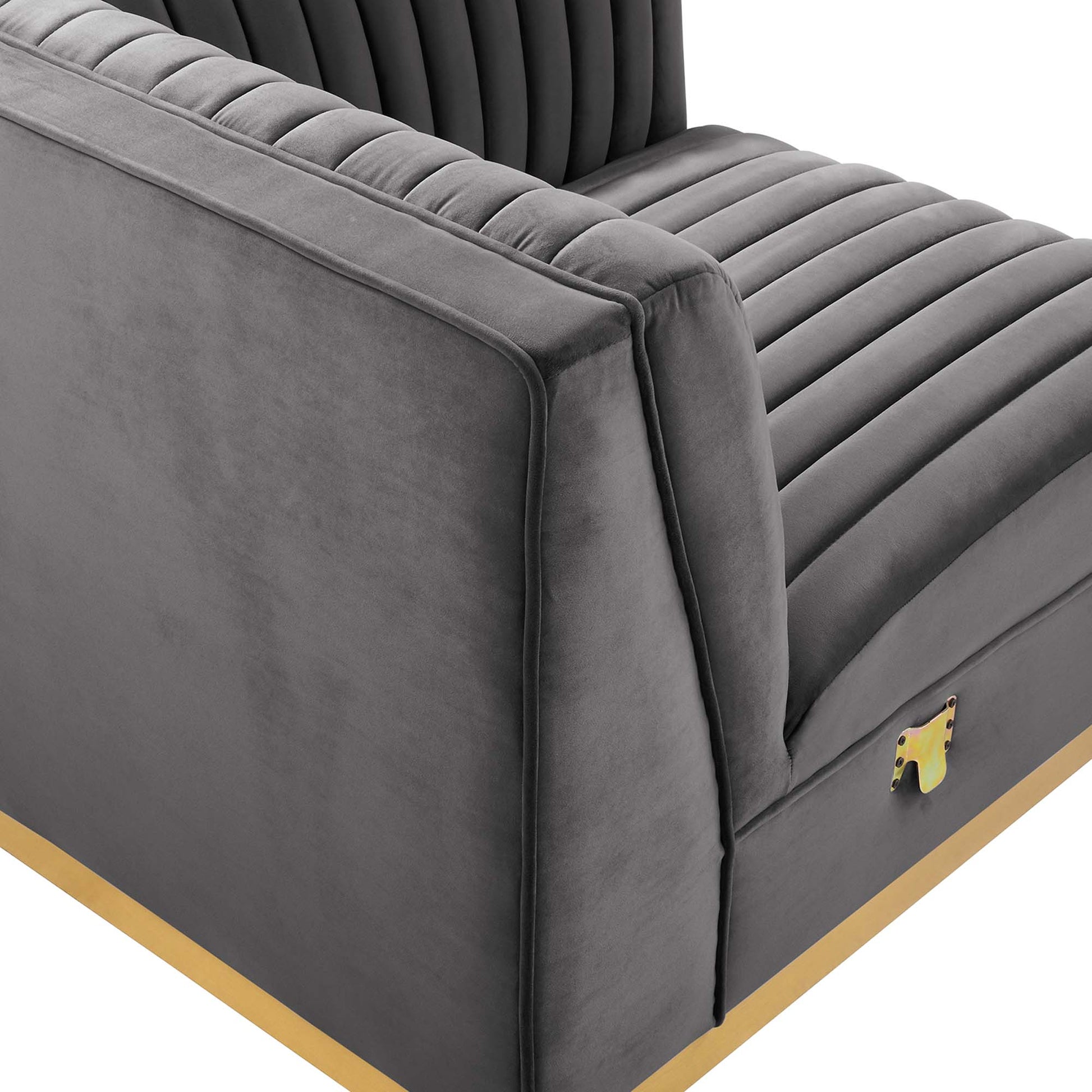 Gray velvet chair with vertical channel tufting, padded arms, and a gold base trim.