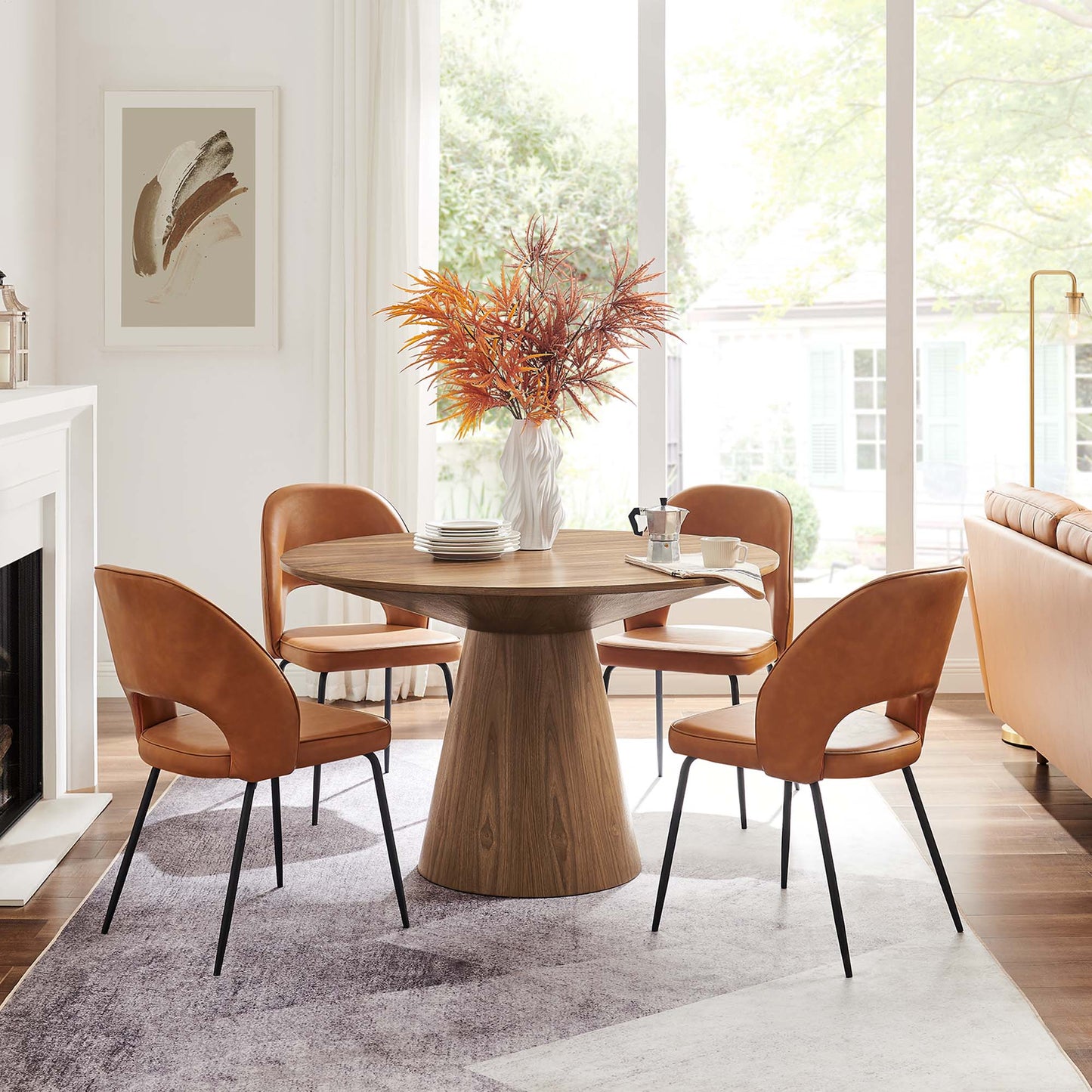 Round walnut pedestal dining table with four caramel leather chairs and an autumn bouquet centerpiece