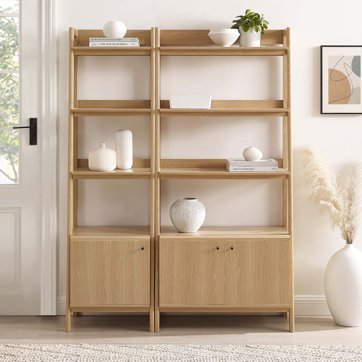 Pair of light oak open-shelving bookcases with bottom cabinets, styled with vases and a plant.