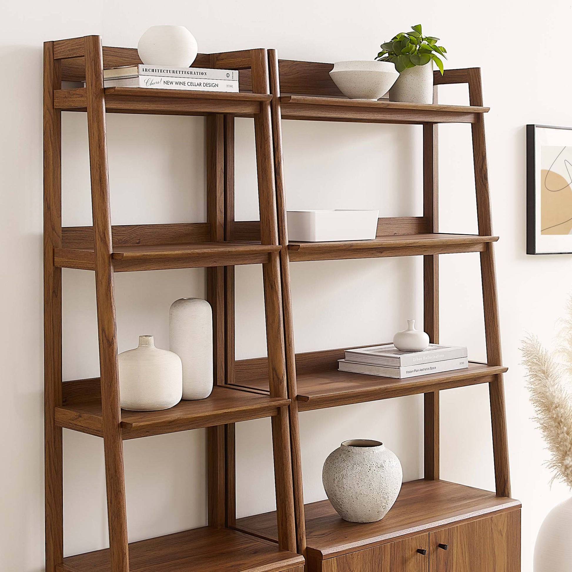Walnut ladder bookshelf with five open shelves and a bottom cabinet; decorated with white vases, bowls, books and a plant.