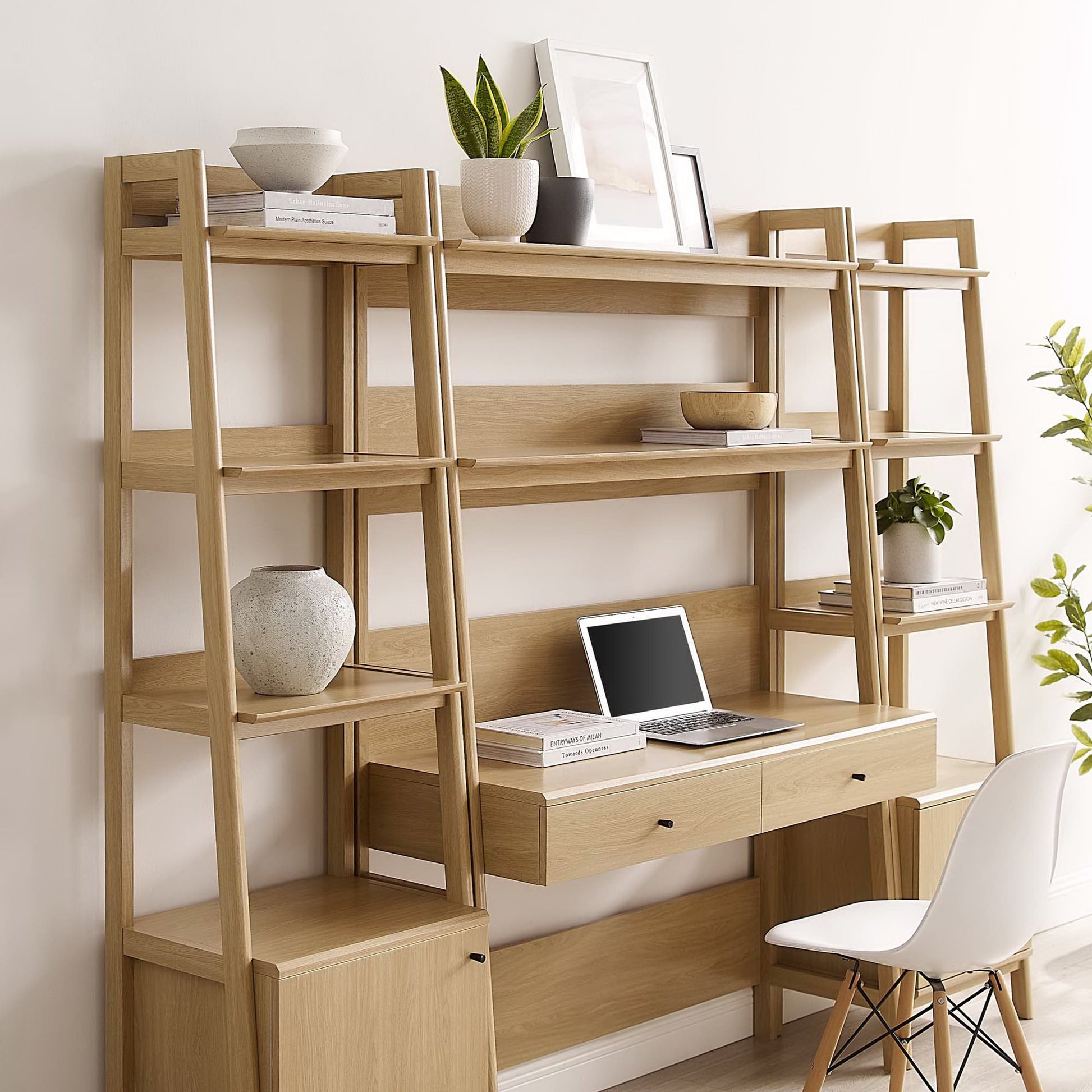 Light oak wood ladder-style shelving with central desk and two-drawer unit; home office setup with laptop, plants.