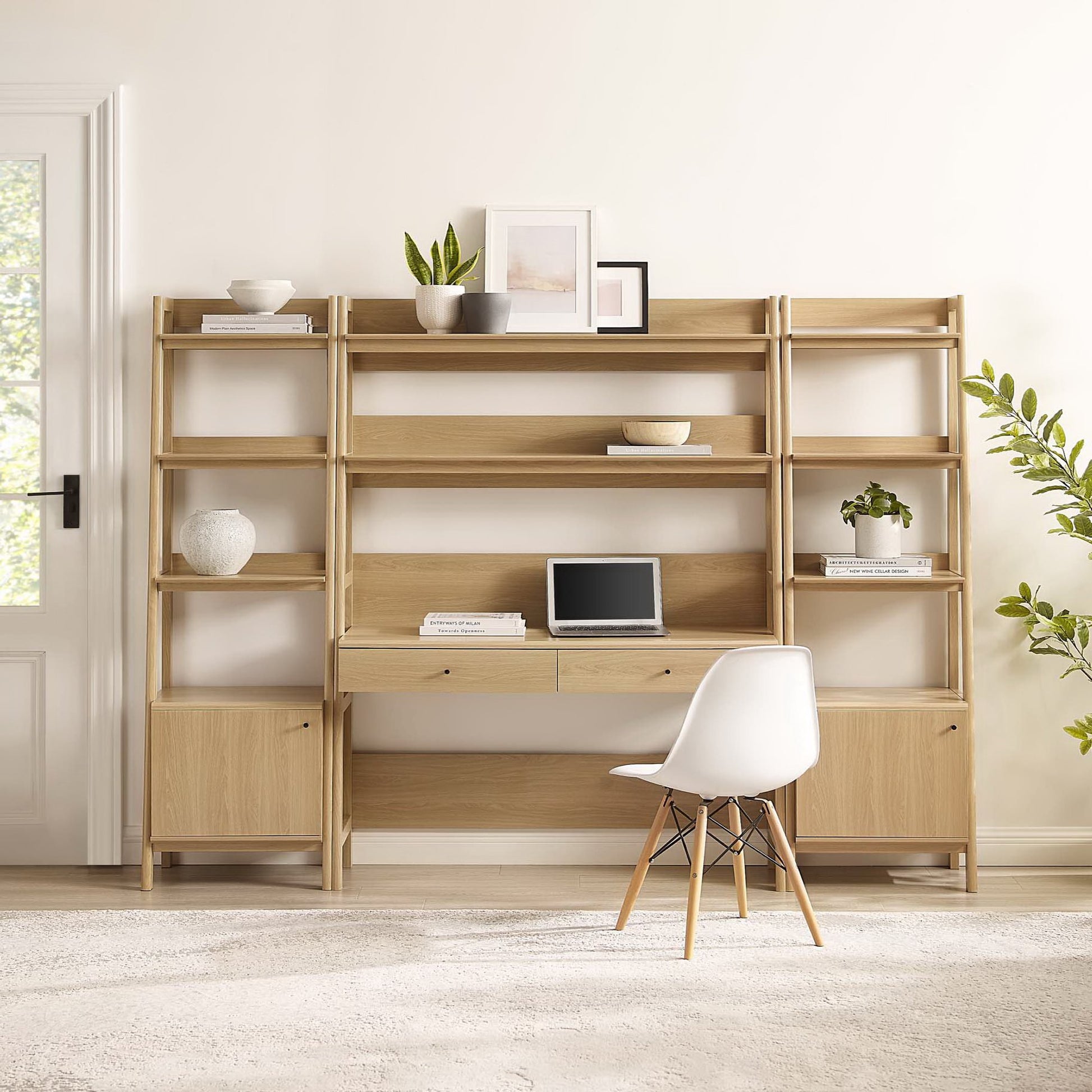 Oak modular shelving unit with built-in desk, open cubbies, small cabinets, white chair, potted plants and framed art