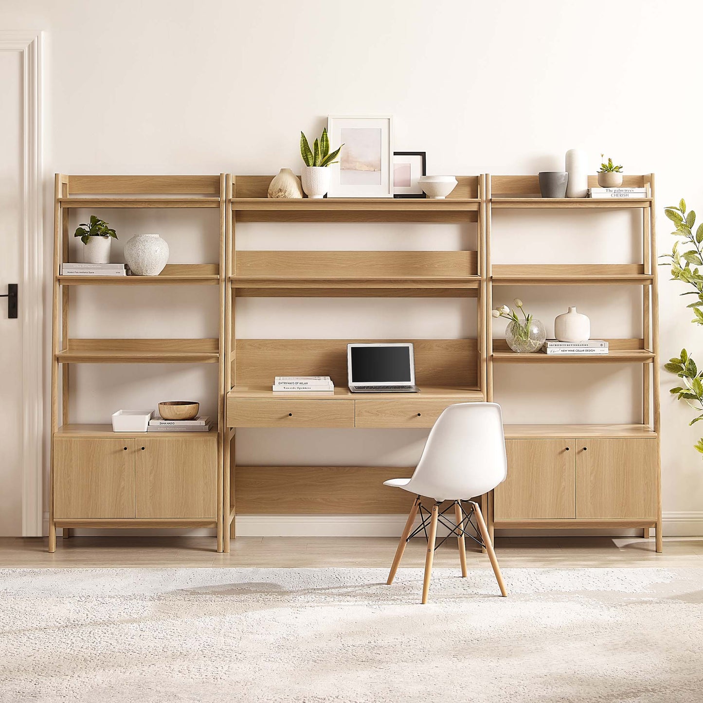 Oak wood office desk and bookshelf set with open shelves and cabinets, laptop area, white chair, and plants in a bright living room.