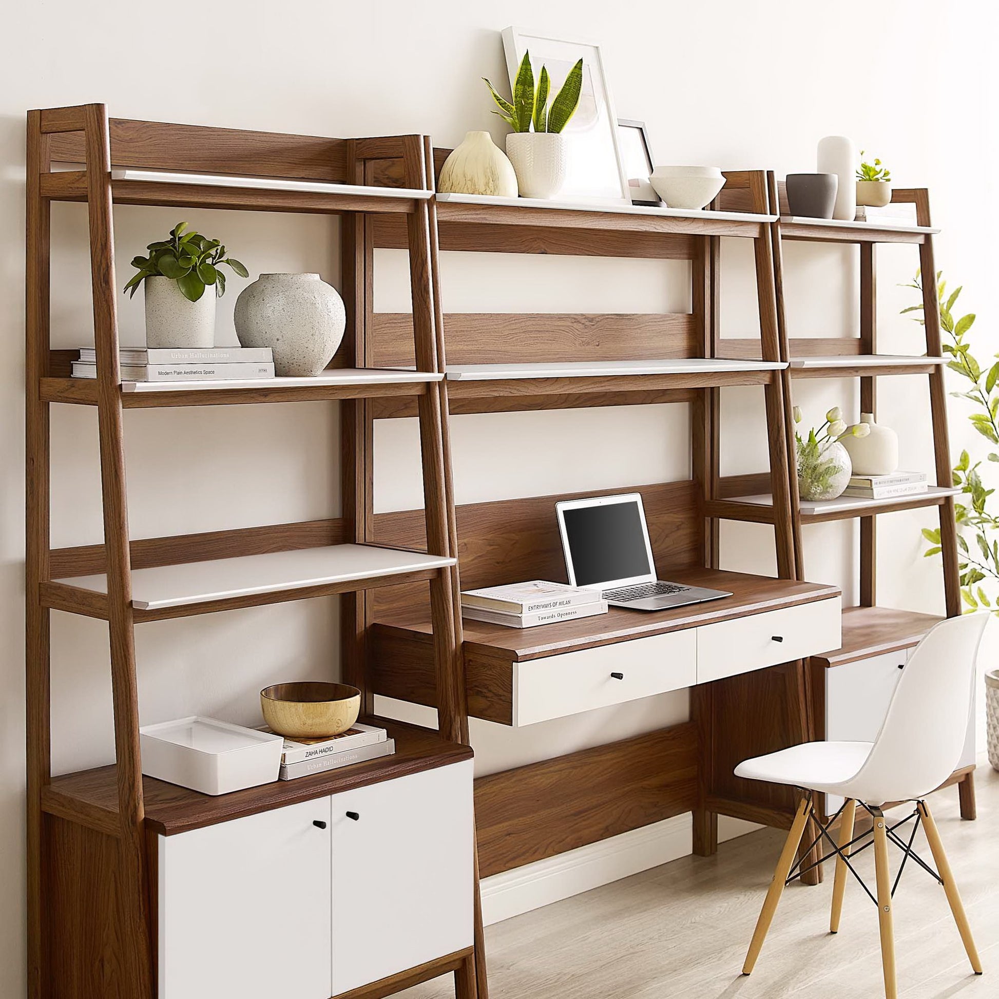 Walnut wood desk with white shelves and drawers, open shelving with plants, laptop on the desk, white chair.