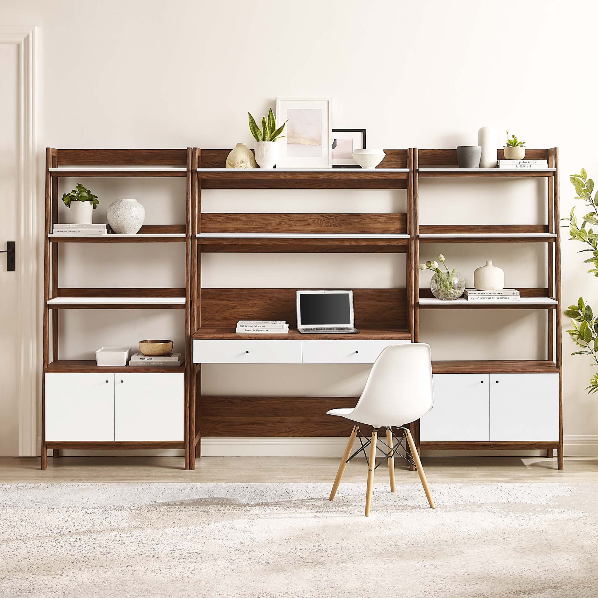 Walnut wood modular shelving with white storage cabinets, central desk, white chair, and plants.
