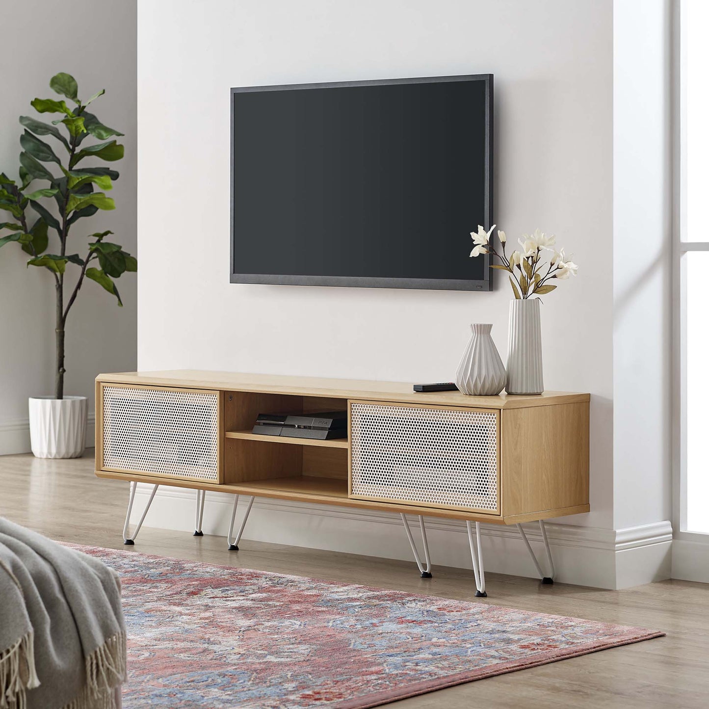 Oak wood media console with woven rattan doors, open shelf, slim metal legs, TV above, decorative vases.