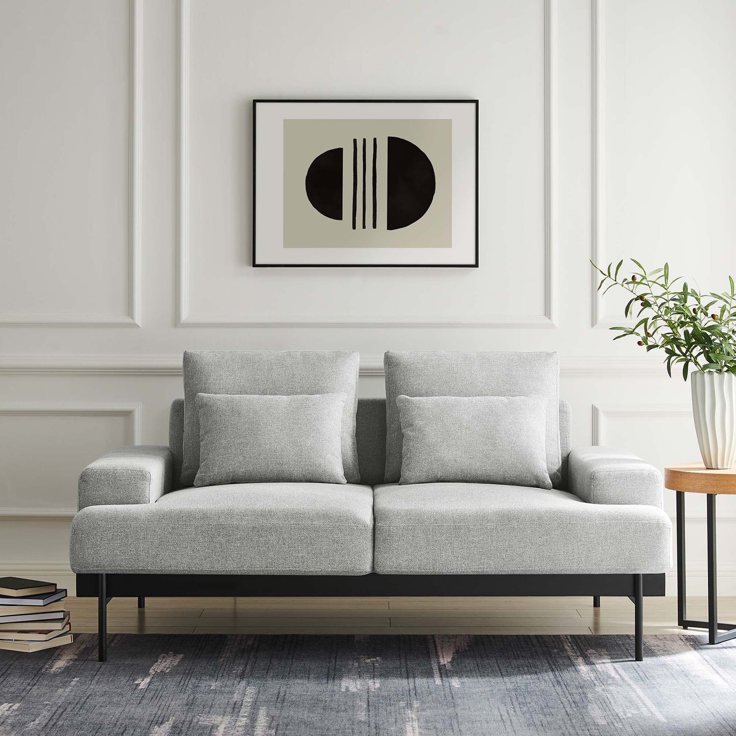 Light gray contemporary loveseat with two cushions, black metal legs, abstract art, plant, books, and blue-gray rug.