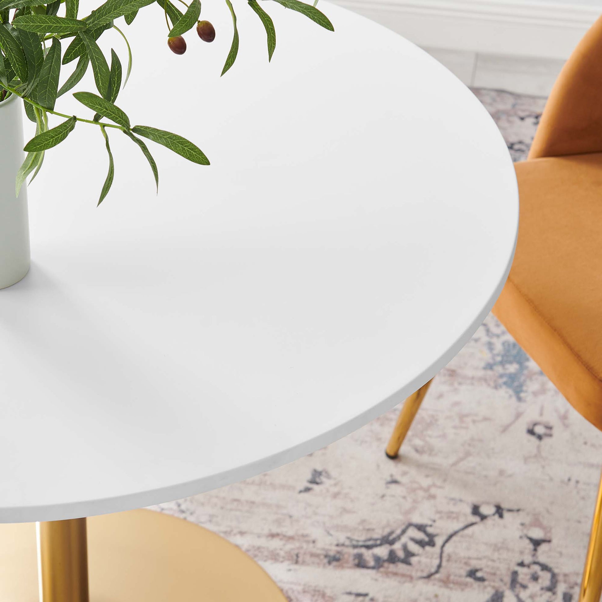 White dining table with gold legs, vase of greenery, and a yellow chair nearby in a mid-century modern setting.