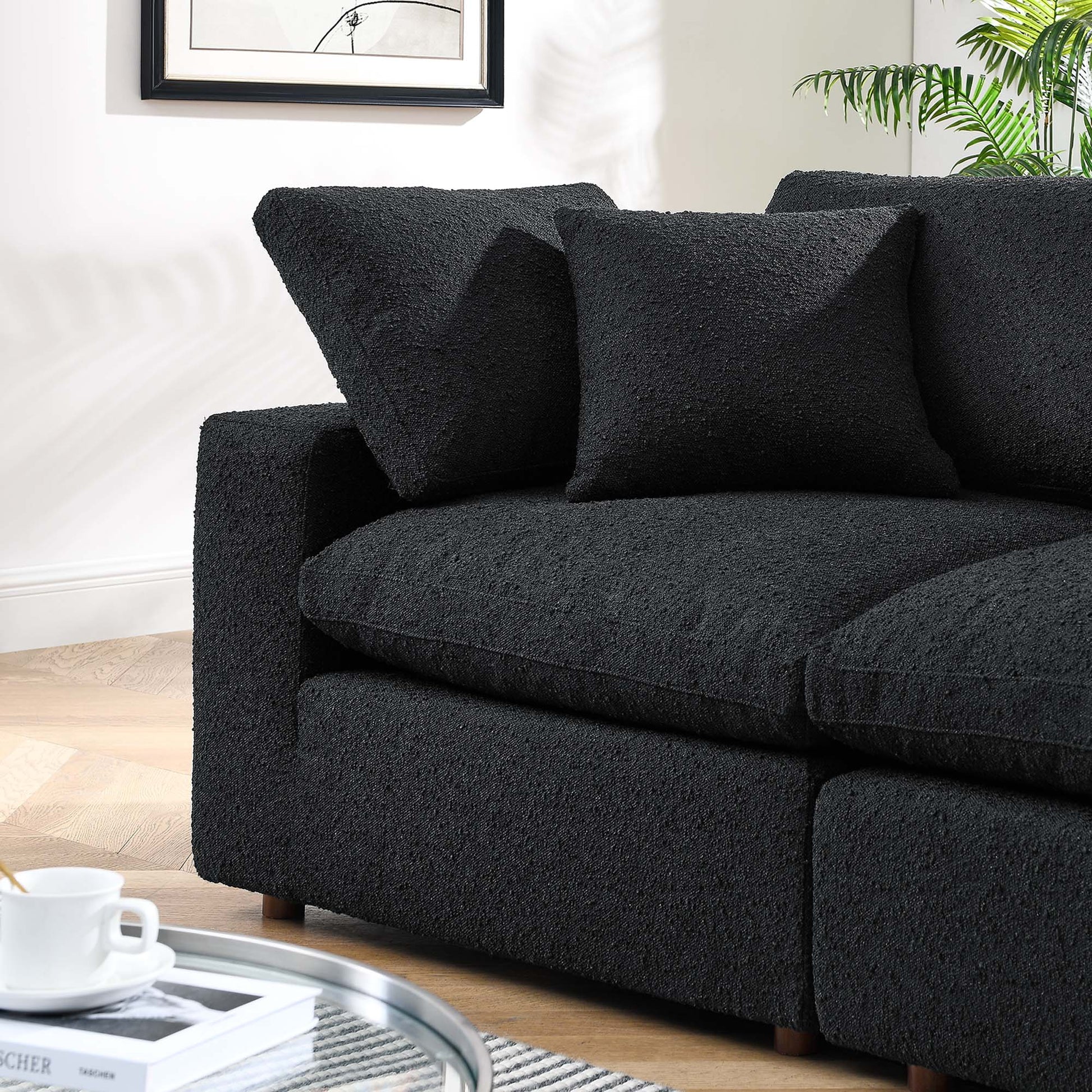 Charcoal black textured fabric loveseat with two matching cushions on a light wood floor, plant in corner.
