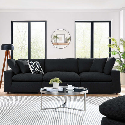Black boucle fabric 3-seater sofa with cushions, round glass coffee table on a striped rug in a bright modern living room.