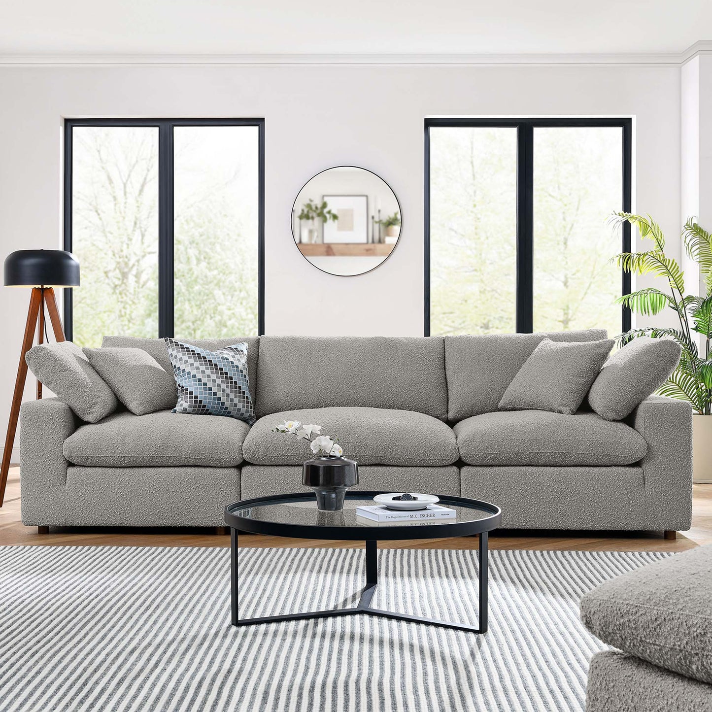 Gray fabric sofa with cushions in a bright modern living room; round black coffee table, striped rug, plants.