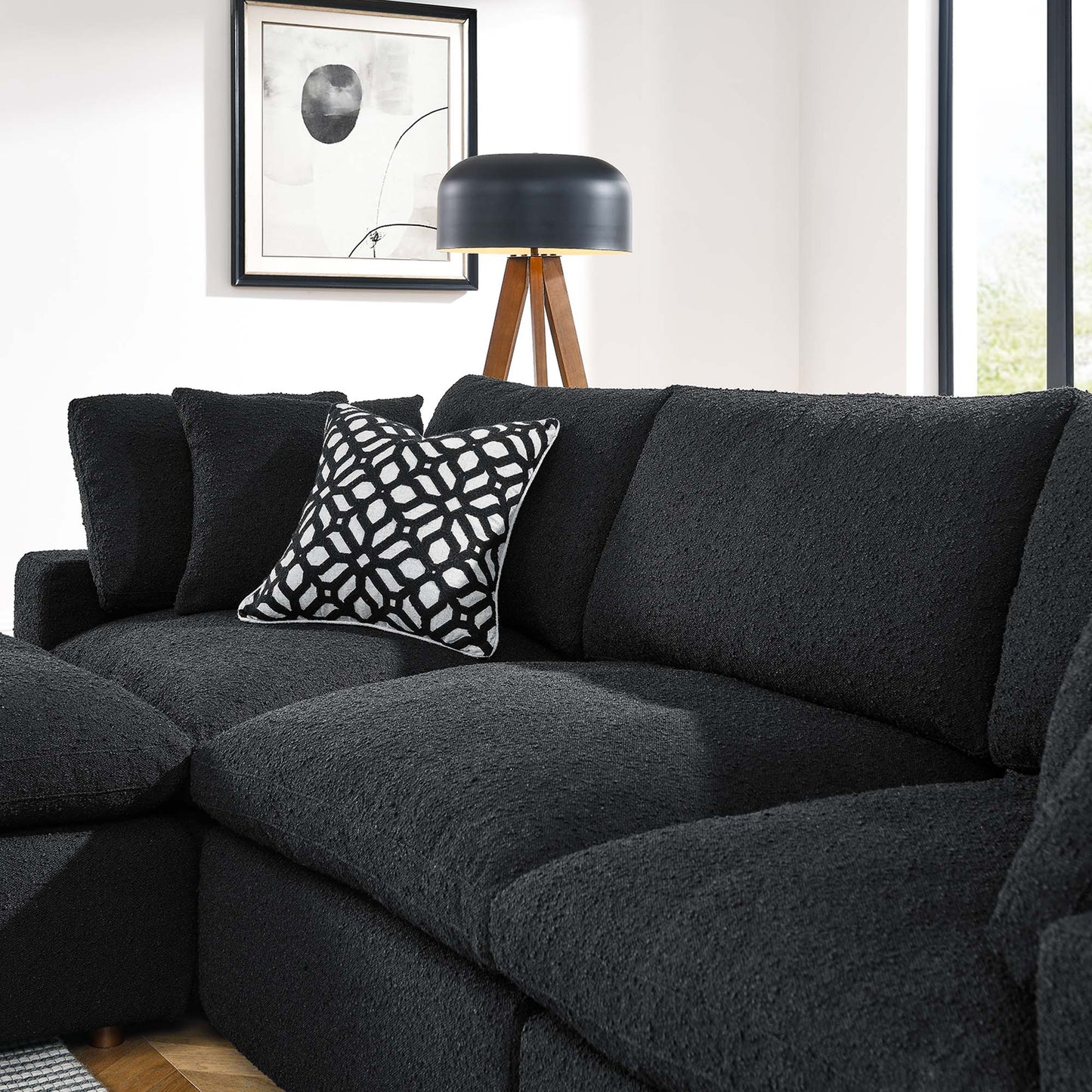 Charcoal textured sectional sofa with a black-and-white geometric pillow, wood tripod lamp, and framed abstract art.