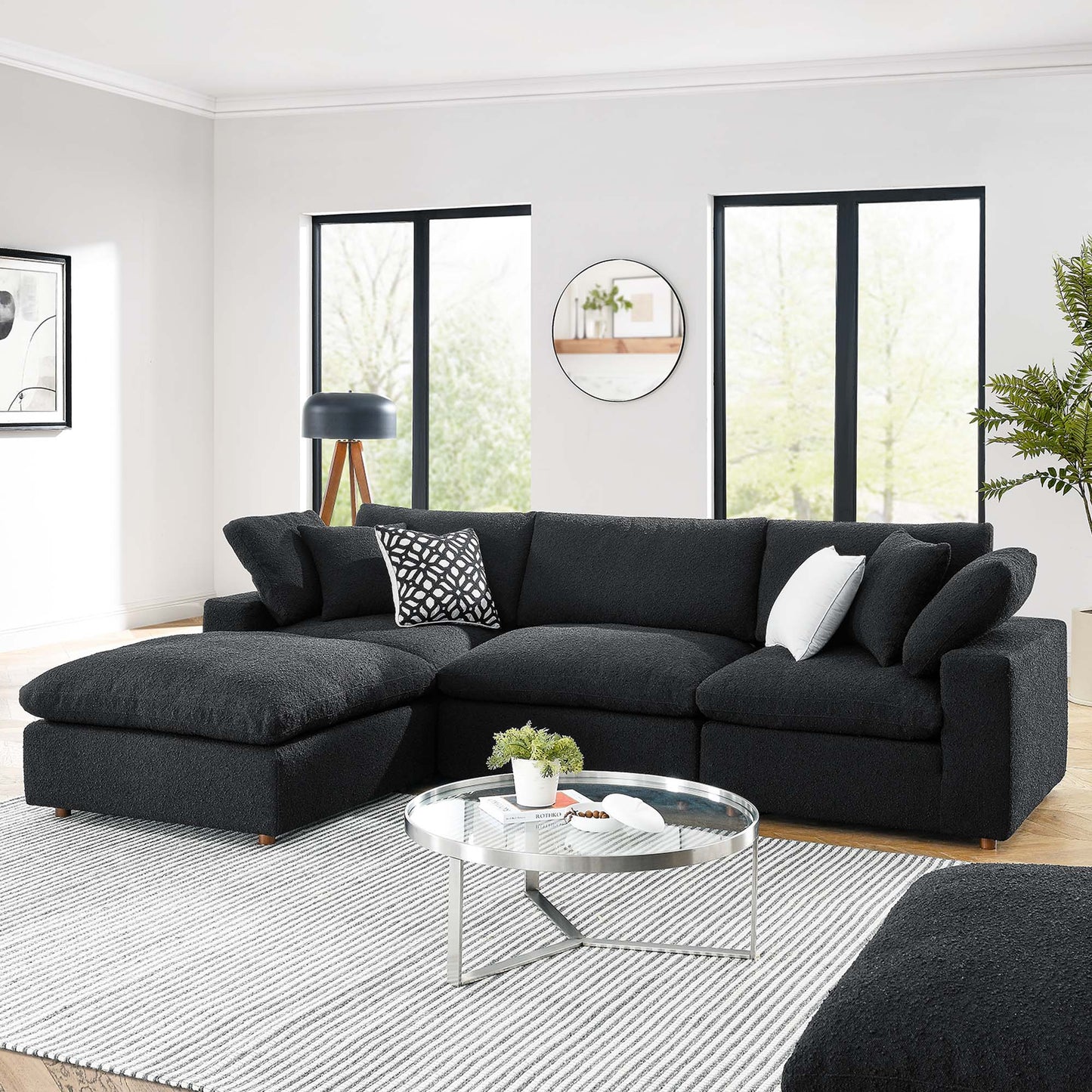 Charcoal fabric L-shaped sectional with chaise, round glass coffee table, modern living room with black-framed windows.