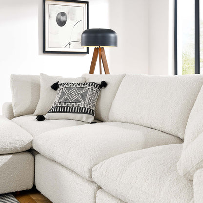 Ivory boucle sectional sofa with a black-and-white tassel-edged throw pillow, tripod floor lamp, and abstract wall art.