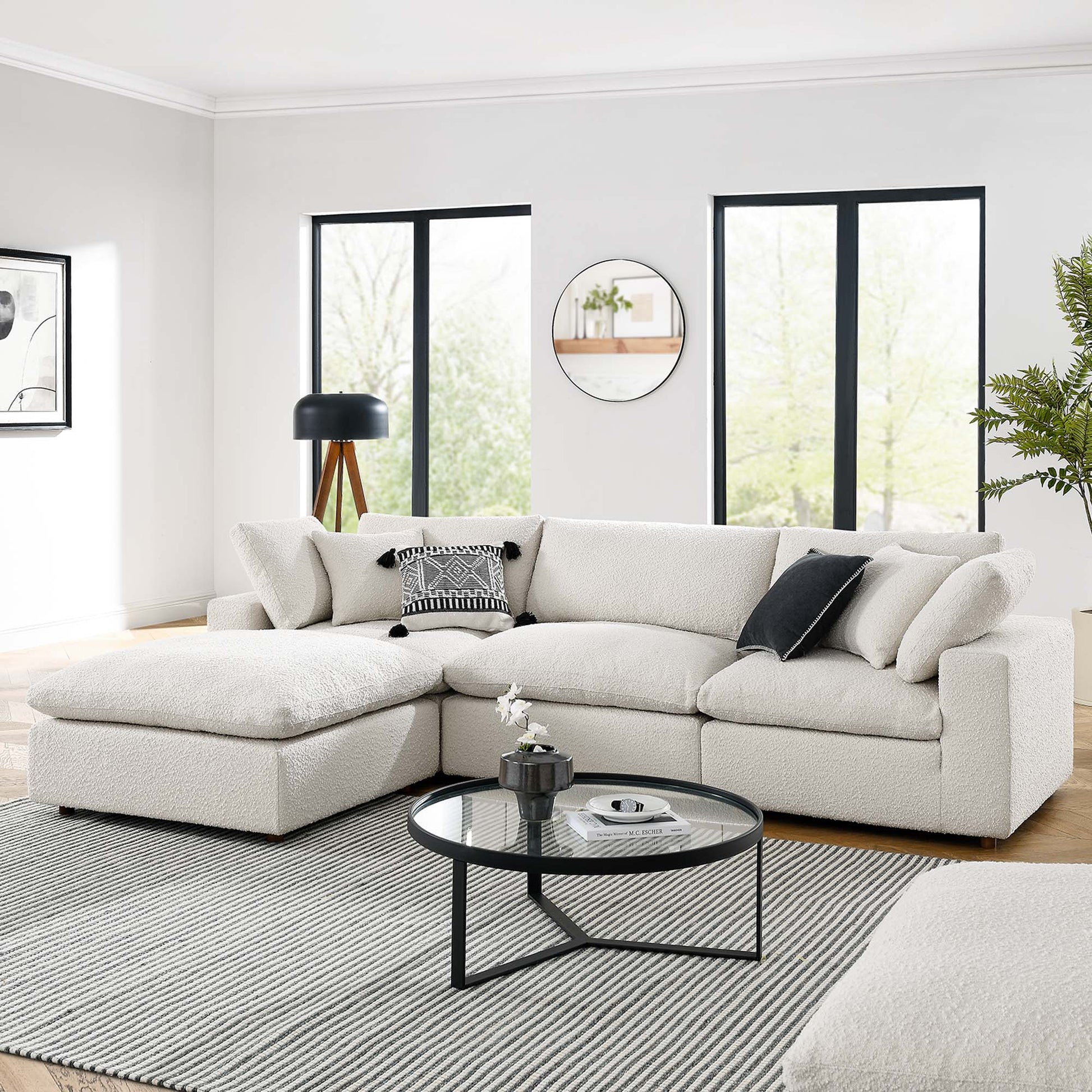 Ivory fabric modular sectional with chaise in a bright modern living room; round glass coffee table, black metal frame, striped rug.