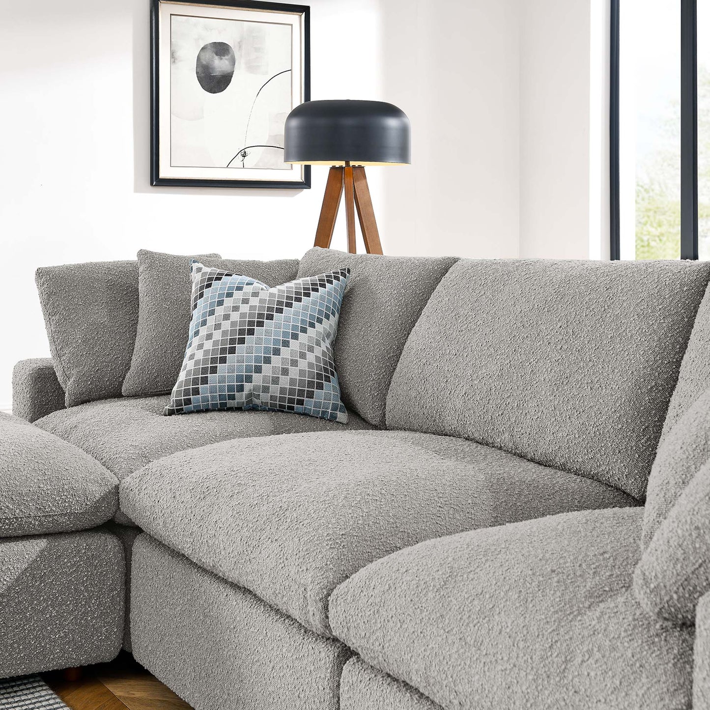 Light gray boucle sectional sofa with a blue-gray geometric pillow and a black-shade tripod floor lamp in a living room.