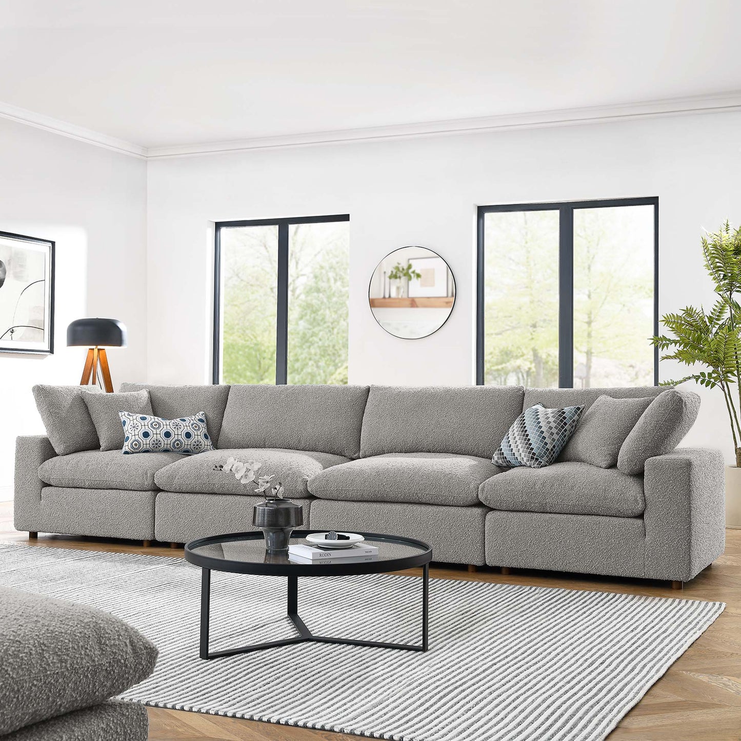 Light gray fabric 4-seater sofa, round black coffee table, striped rug, modern living room setup.