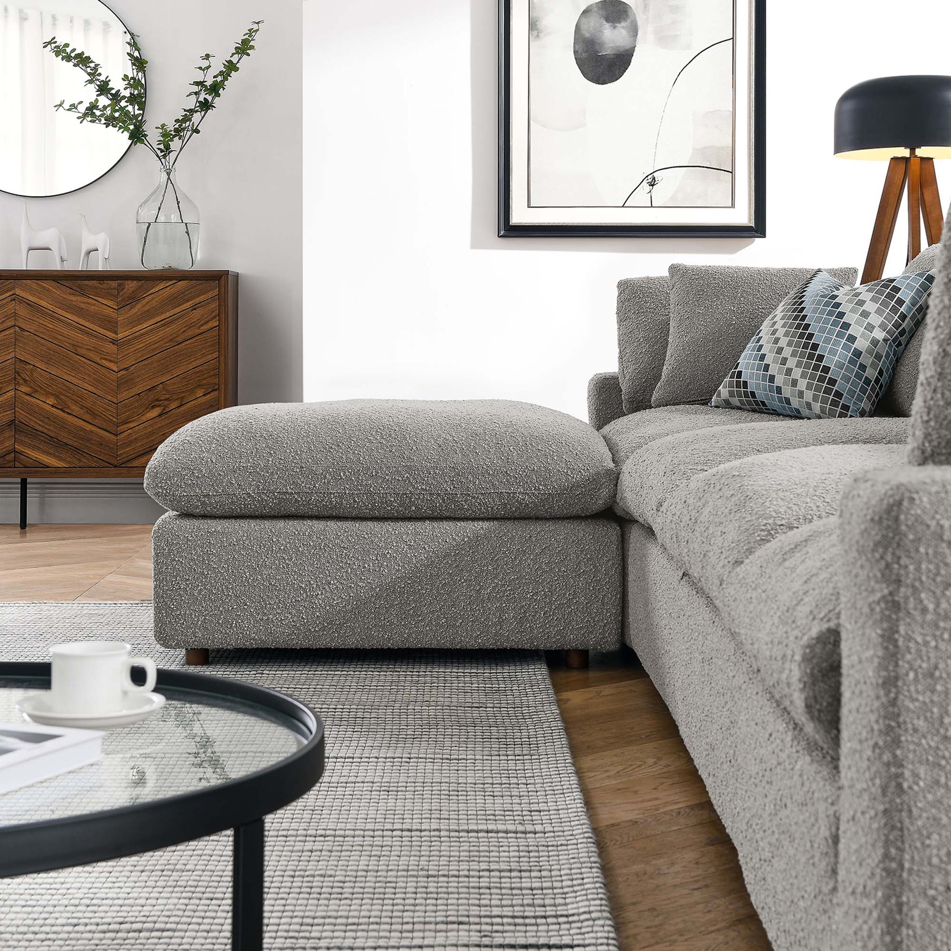 Modern grey textured fabric sectional with chaise, glass coffee table, chevron wood sideboard, gray rug, black-framed art.