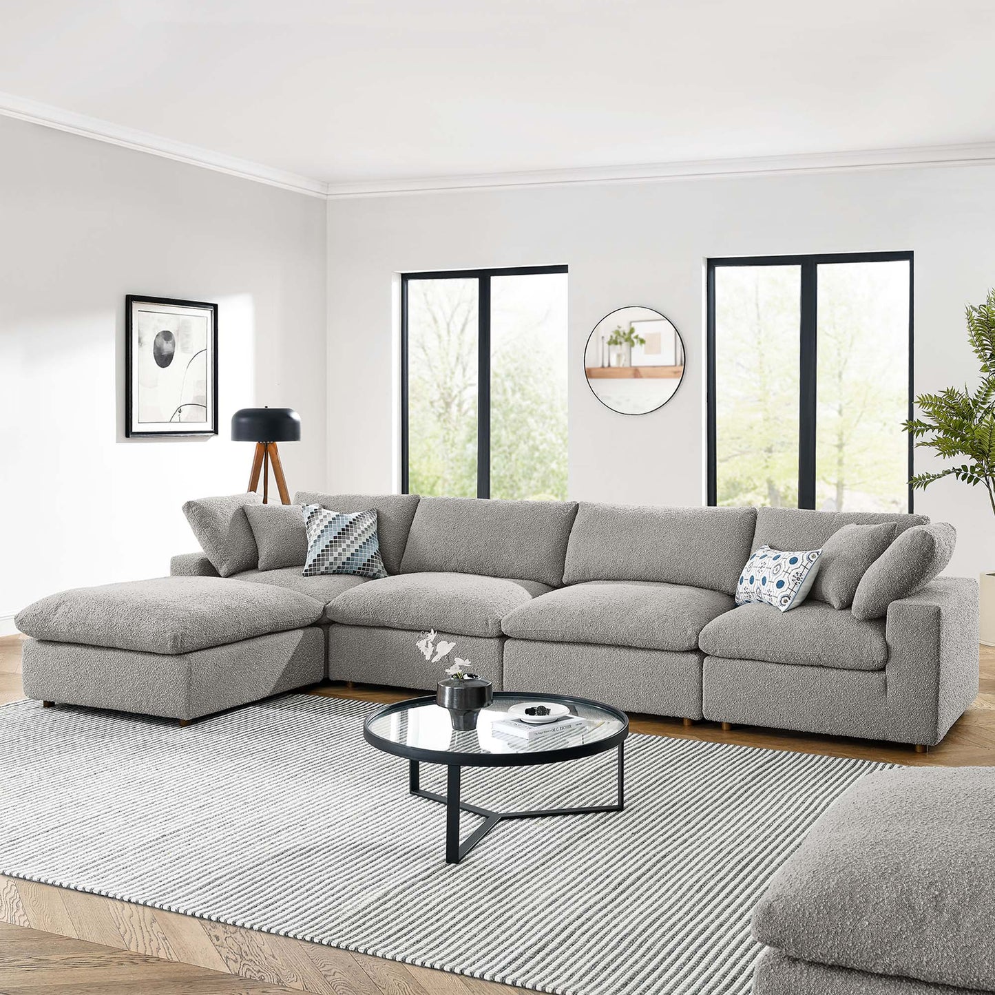 Light gray sectional sofa with chaise, circular glass coffee table on a striped gray rug in a bright modern living room.