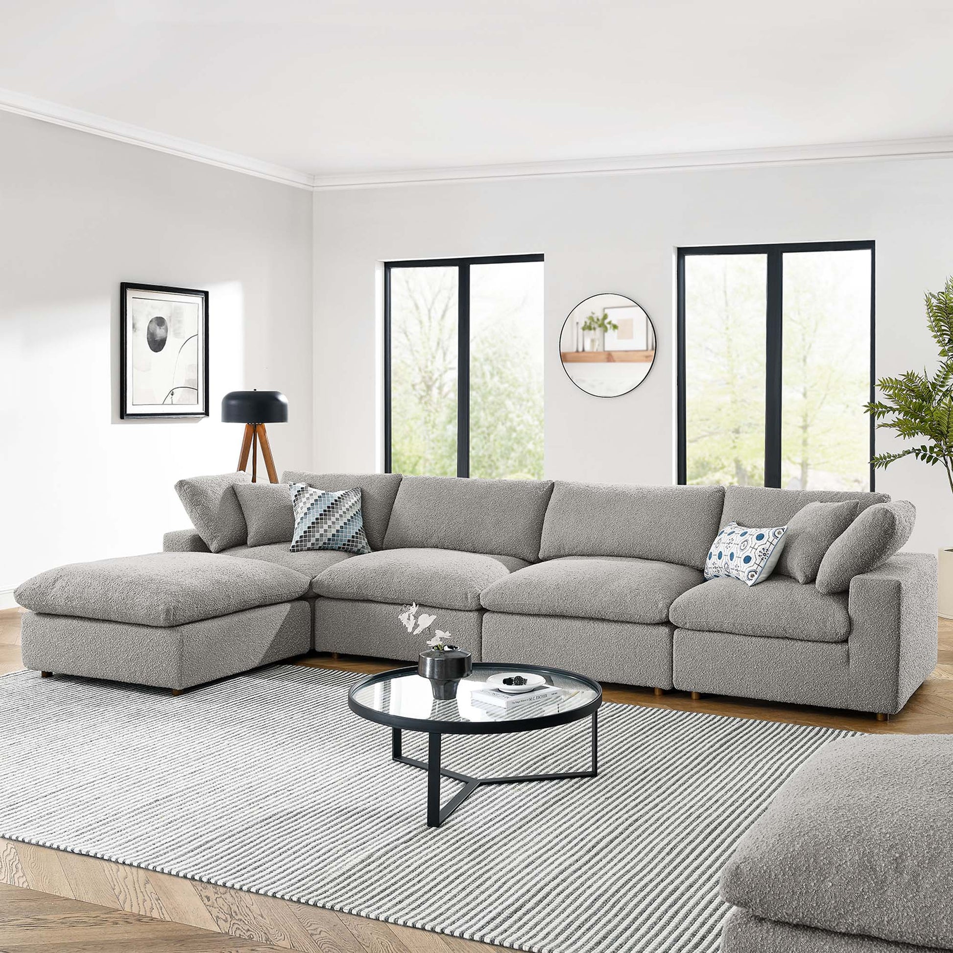 Light gray sectional sofa with chaise, circular glass coffee table on a striped gray rug in a bright modern living room.