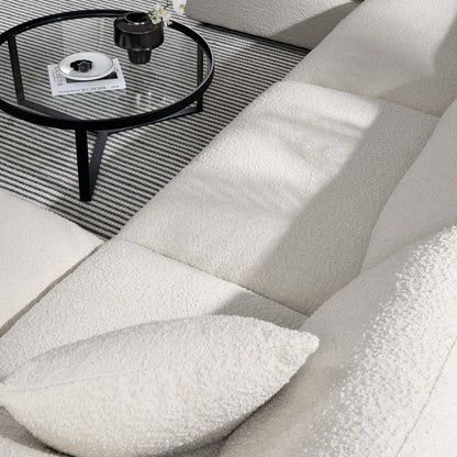 Ivory boucle sectional sofa with matching pillow, round glass-top black metal coffee table on striped grey rug.