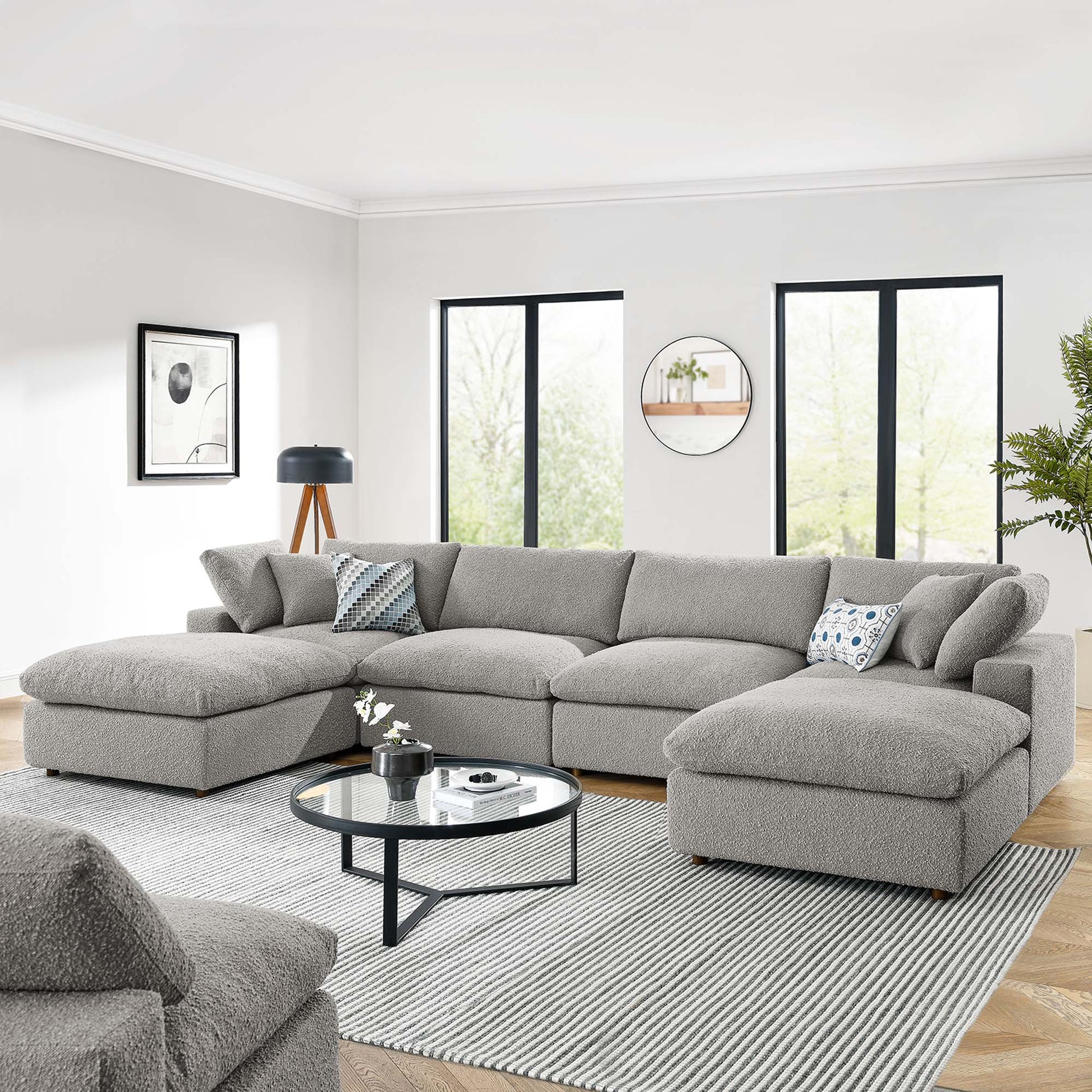 Light gray L-shaped sectional sofa with chaise in a bright modern living room; round glass coffee table and striped rug.