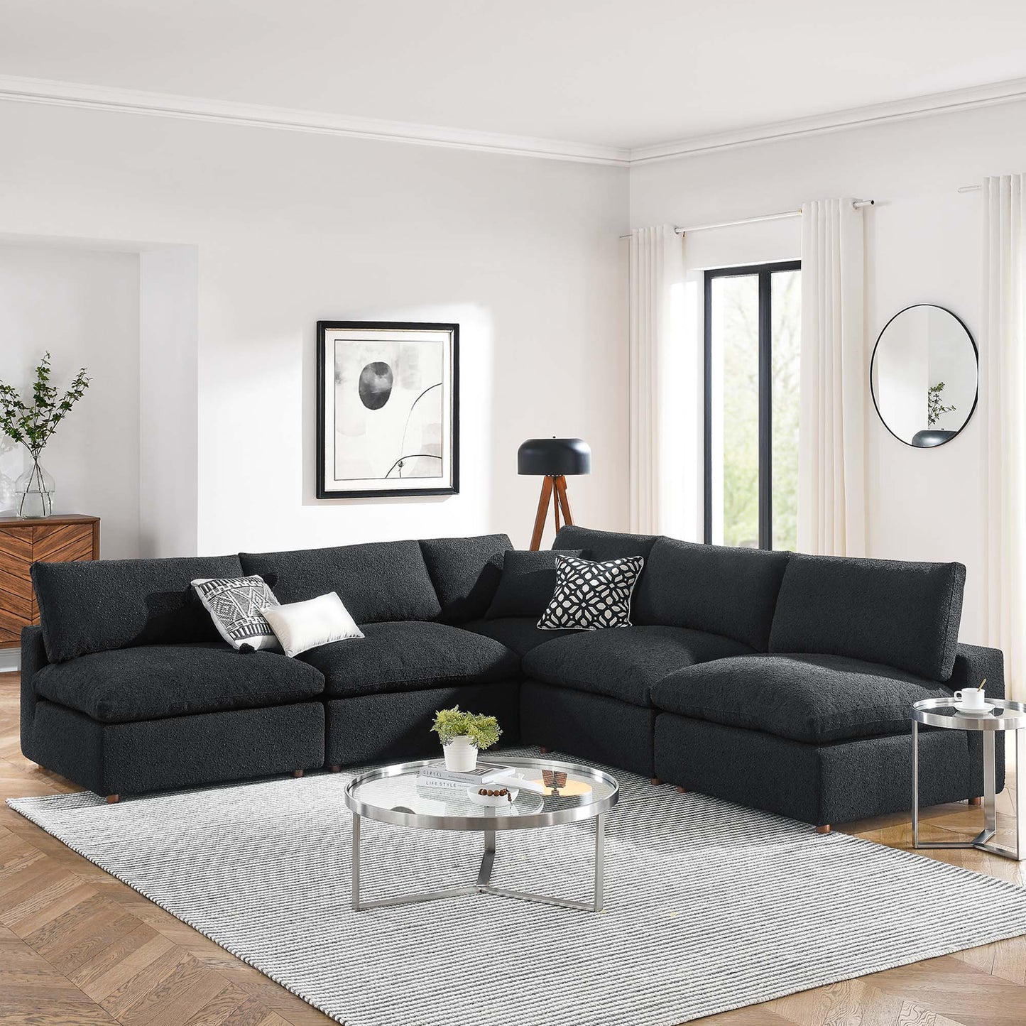 Black boucle fabric sectional with chaise; modern living room featuring glass coffee table & round side table.