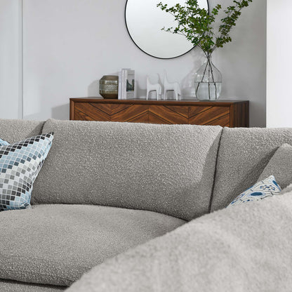Textured light gray sectional sofa with blue geometric pillow, wooden console, round mirror, and glass vase with greenery.